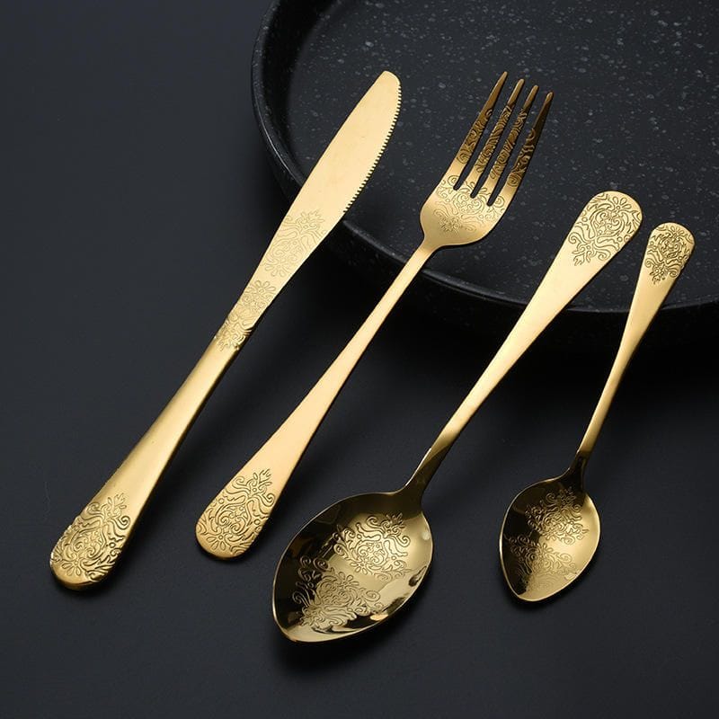 Double flower engraved flatware set in gold finish on a dark plate